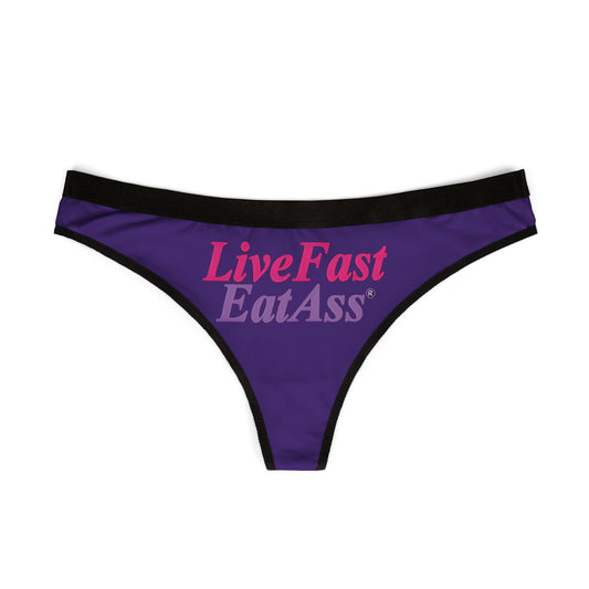 Elegant women's thong panties in vibrant purple featuring the bold graphic design 'Live Fast Eat Ass' in contrasting pink and grey typography.