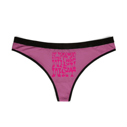 Close-up view of the 'Slippery When Wet' thong, highlighting the iconic neon-pink typeface against a rich pink background, symbolising playful sensuality.