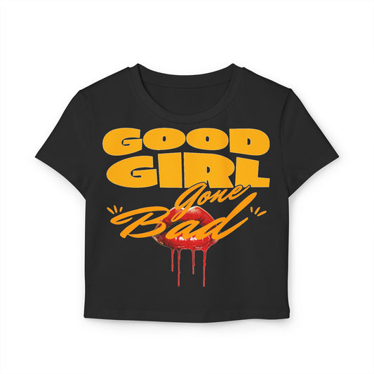 Chic black crop tee displaying the audacious ‘Good Girl Gone Bad’ slogan in bold orange-yellow text, complemented by a captivating red lips graphic for a seductive flair.