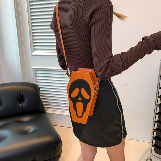 Luxurious Halloween Coffin-shape Shoulder Bag in vibrant orange, adorned with a striking ghost face, perfectly styled with a sleek black skirt.