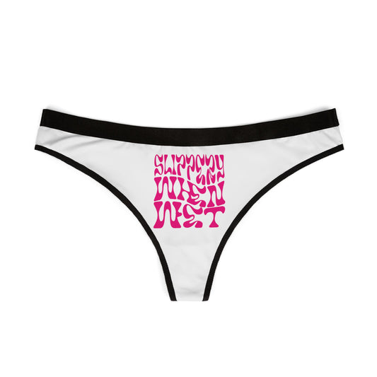 Close-up view of 'SLIPPY WHEN WET' thong panties featuring vibrant pink typography against a classic white backdrop, embodying a chic and bold lingerie style.
