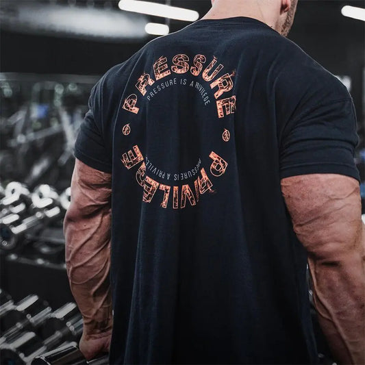 Close-up of the back design of the Men's Summer Gym Sports Tee, highlighting the inspirational text 'Pressure is a Privilege', worn by a muscular man in a gym environment.