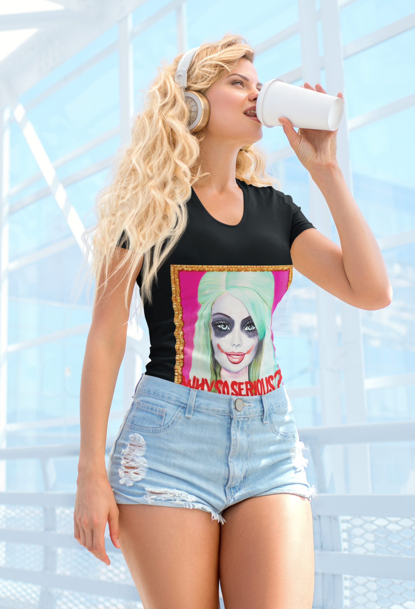 Model showcasing the 'Why So Serious' Joker Barbie women's graphic slim fit t-shirt in black, featuring striking pop art imagery and dramatic lettering, complemented by distressed denim shorts and chic headphones in a modern, bright setting.