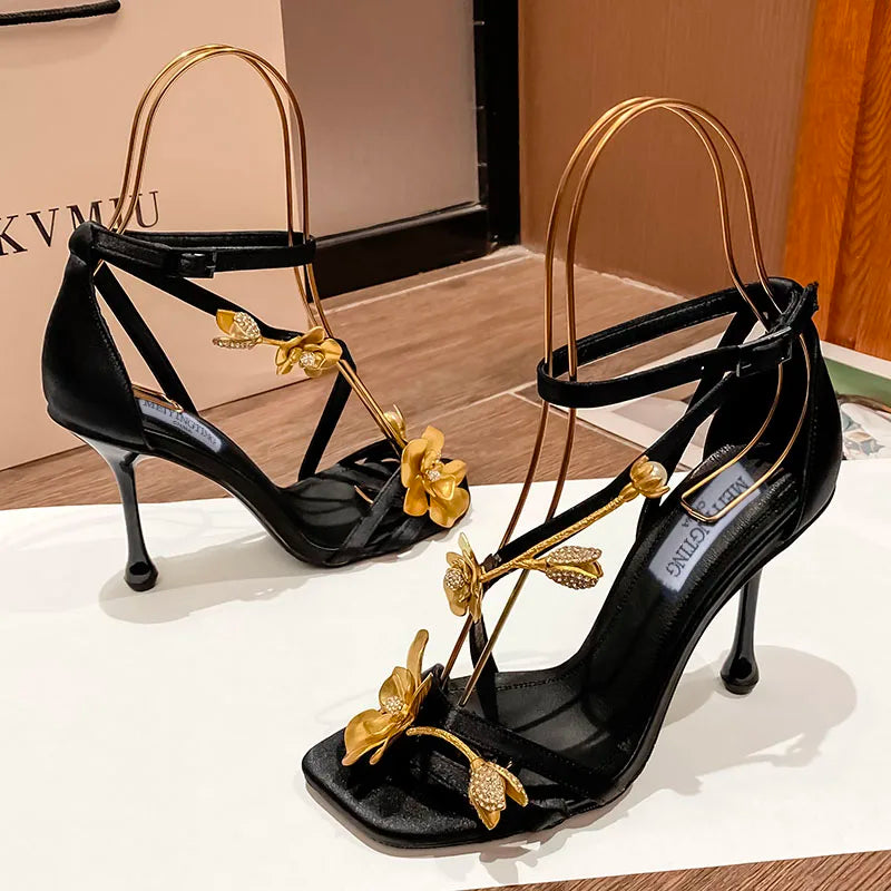 Chic black high heel sandals with a sumptuous gold flower metal detail, a must-have for luxury fashion enthusiasts at formal occasions.
