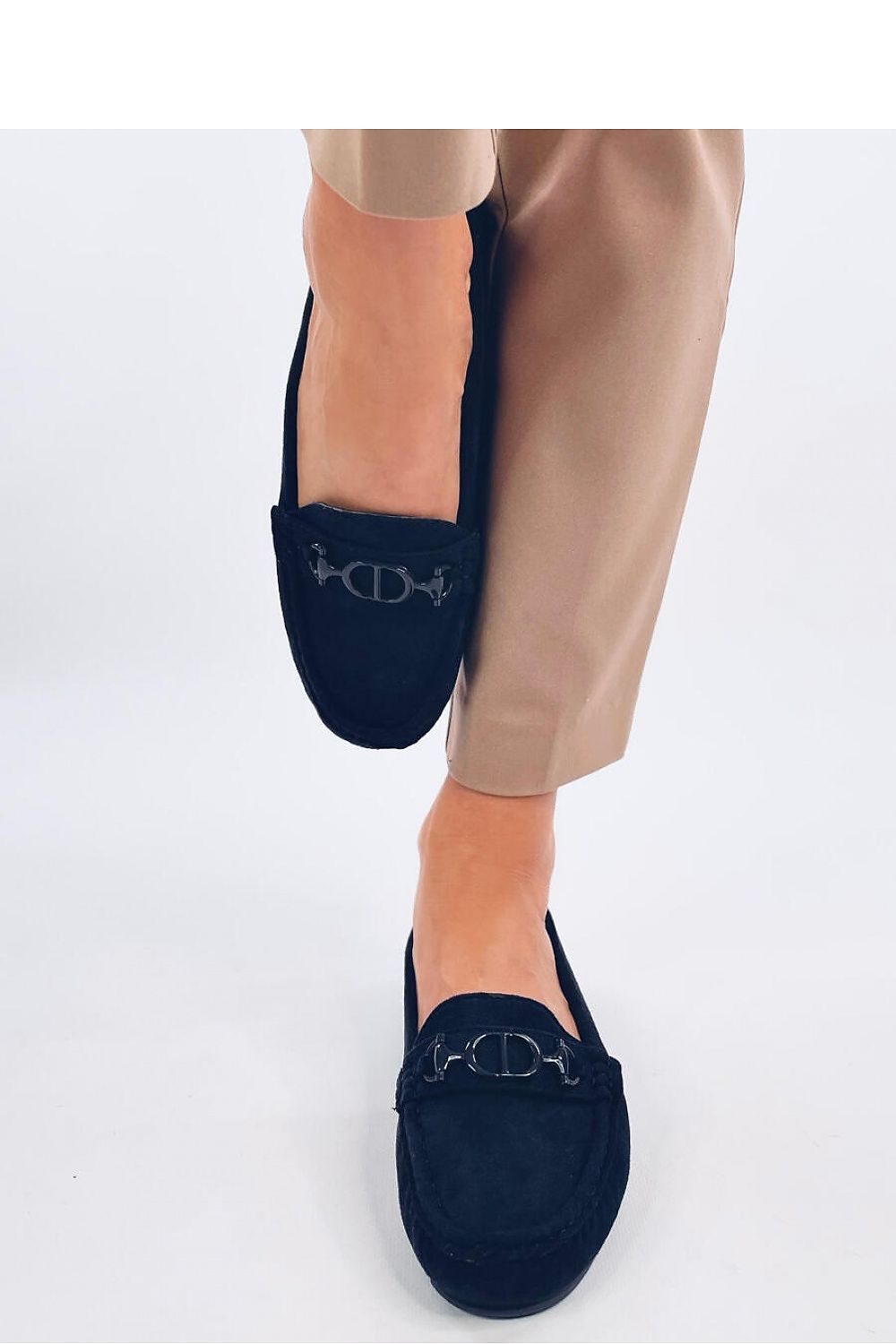 Luxury women's suede moccasins in black, featuring unique stitching and a decorative buckle, showcased on a model's foot, paired with stylish beige trousers. By Inello.