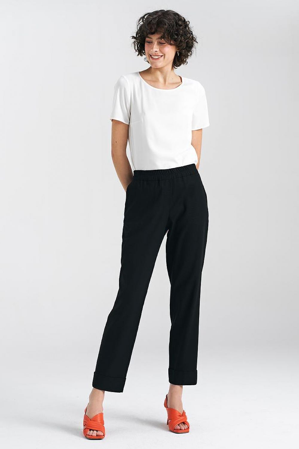 Luxury women's relaxed fit trousers in black by Nife, featuring a straight leg and cuffs, styled with a simple white top and vibrant red sandals, showcasing comfort and elegance.