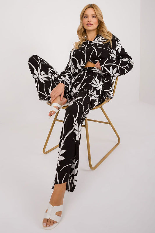 Sophisticated Lakerta cotton casual outfit, model seated displaying the intricate black and white floral design of the shirt and pants, ideal for casual yet chic occasions.