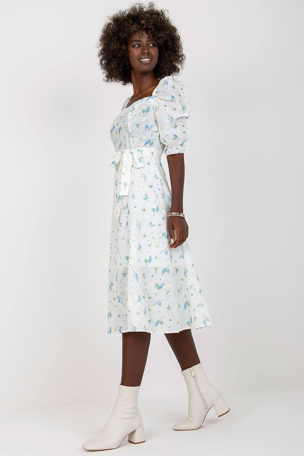 Side profile of the Lakerta floral midi summer dress, emphasising its chic ruffle sleeves and tie belt, elegantly paired with white ankle boots.