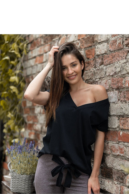 A model showcasing the Sensis Elegant Black and Coffee Two-Piece Pyjama Set with Decorative Waist Tie, featuring a stylish black V-neck t-shirt and coffee-coloured trousers with a decorative waist tie, set against a rustic brick wall background.