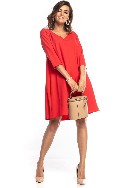 Stylish Tessita trapeze dress in striking red, showcasing 3/4 sleeves and a flattering silhouette, held by a model holding a fashionable handbag.