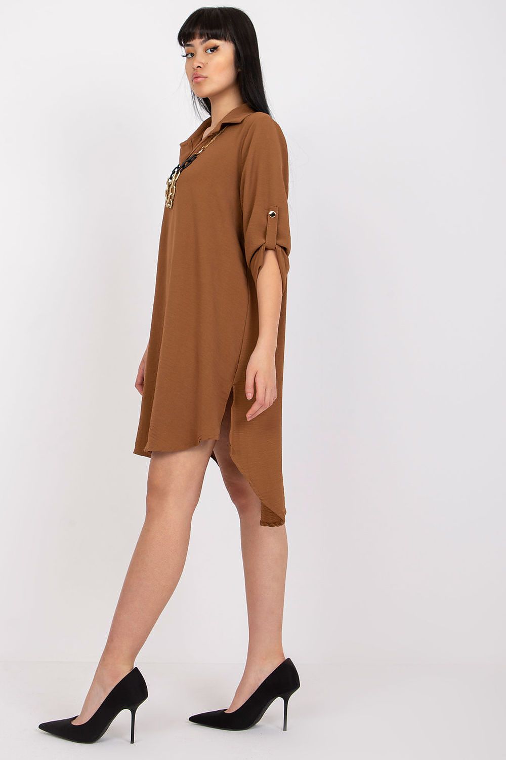 Side view of the Asymmetrical Long Sleeve Dress with Collar by Italy Moda, highlighting its sophisticated design. The model in brown showcases the dress's flowing silhouette and chic collar detail, complemented by stylish black stiletto heels, exuding a sense of luxury and modern elegance.