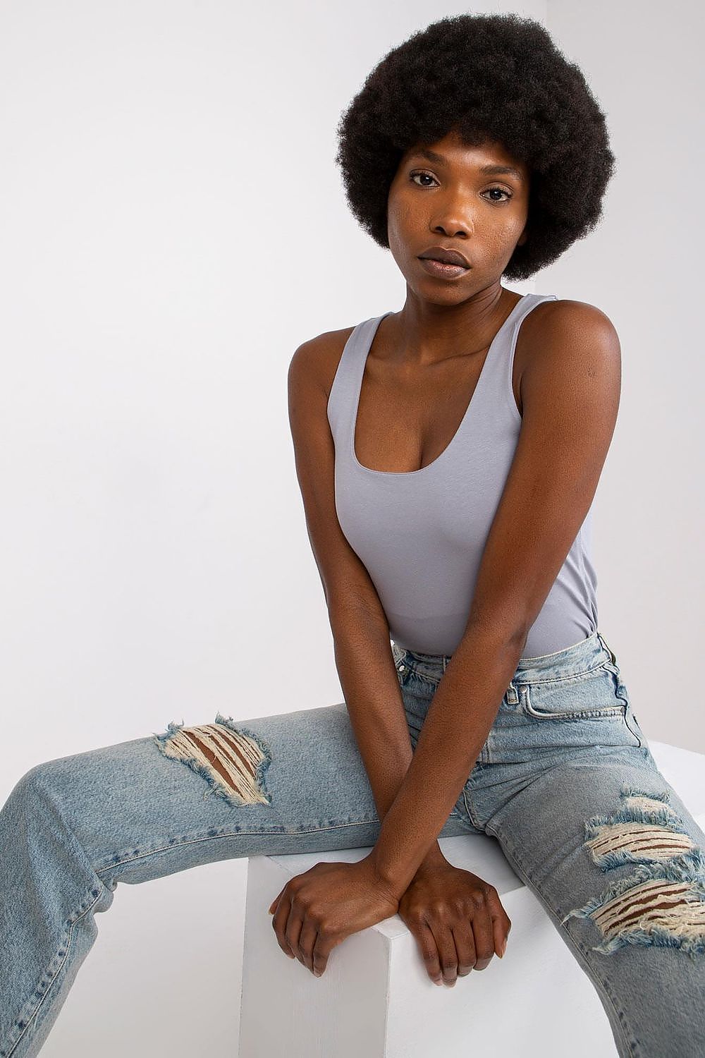 Stylish Strapless T-Shirt for Summer – Comfortable Cotton Blend, Multiple Sizes Available, elegantly posed by a model, capturing the essence of luxury summer wear with a light grey top and fashion-forward distressed jeans.