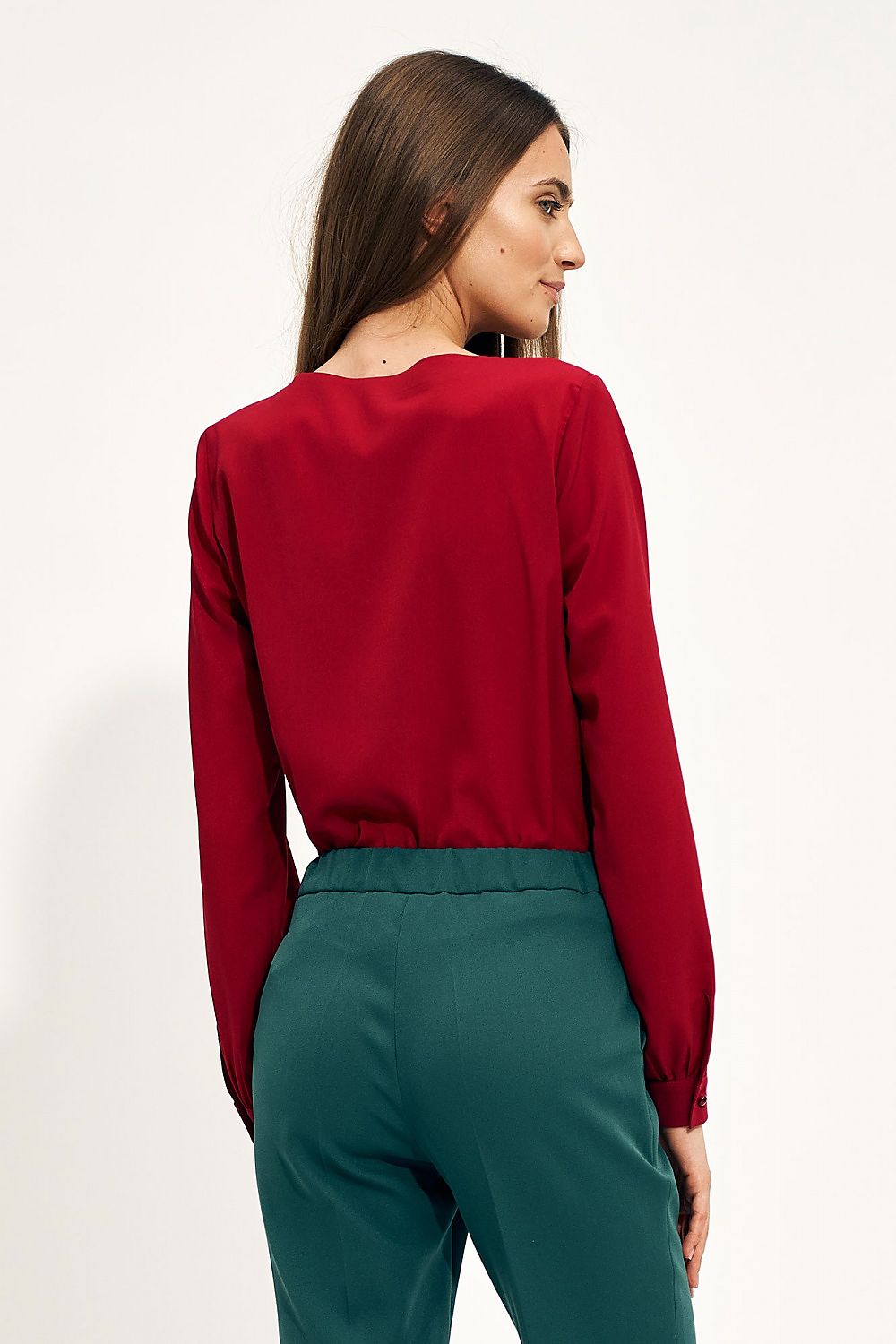 Elegant portrayal of the Nife Teardrop Long Sleeve Shirt with Unique Neckline, featuring a woman showcasing the back view of the rich red blouse paired with stylish green trousers, perfect for sophisticated office styling.