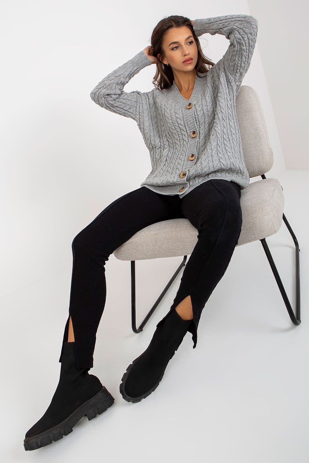 Elegant Women's Long Sleeve Acrylic Cardigan with Button Closure by Rue Paris, featuring a model in a relaxed pose, wearing a grey cardigan with a cable knit design, perfectly paired with modern black attire.