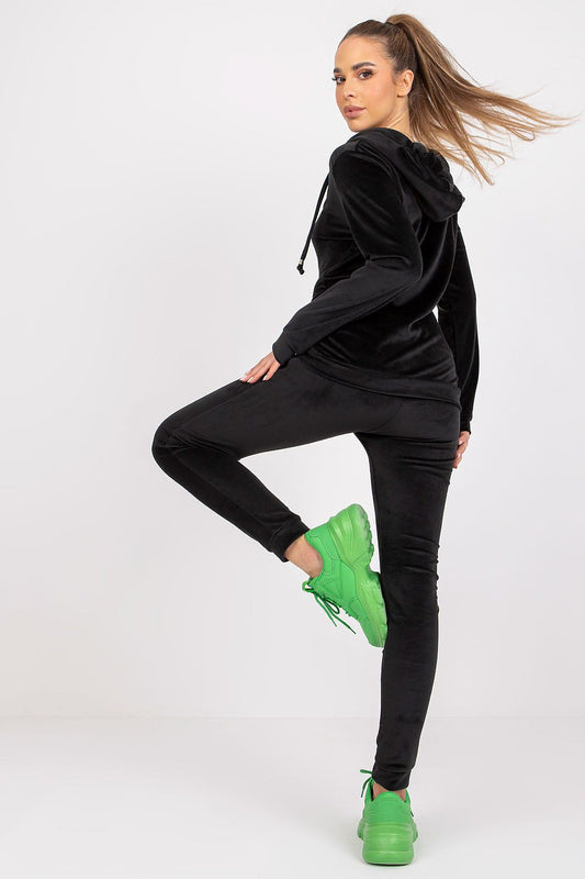 Elegant view of a model in black velour loungewear set featuring a hood and side pockets, complemented by striking green sneakers, highlighting sophisticated leisurewear fashion.