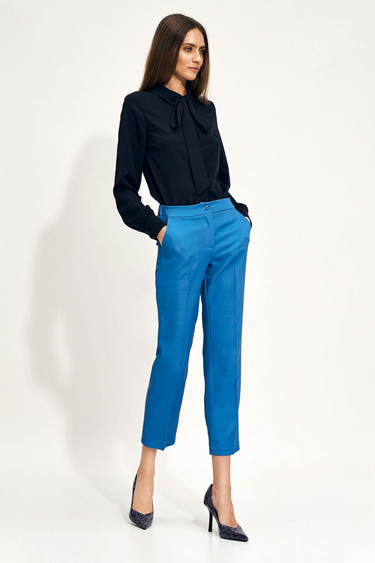 Side view of a model showcasing an elegant black Nife blouse with bow detail, paired with chic blue tailored pants for a sophisticated office outfit.