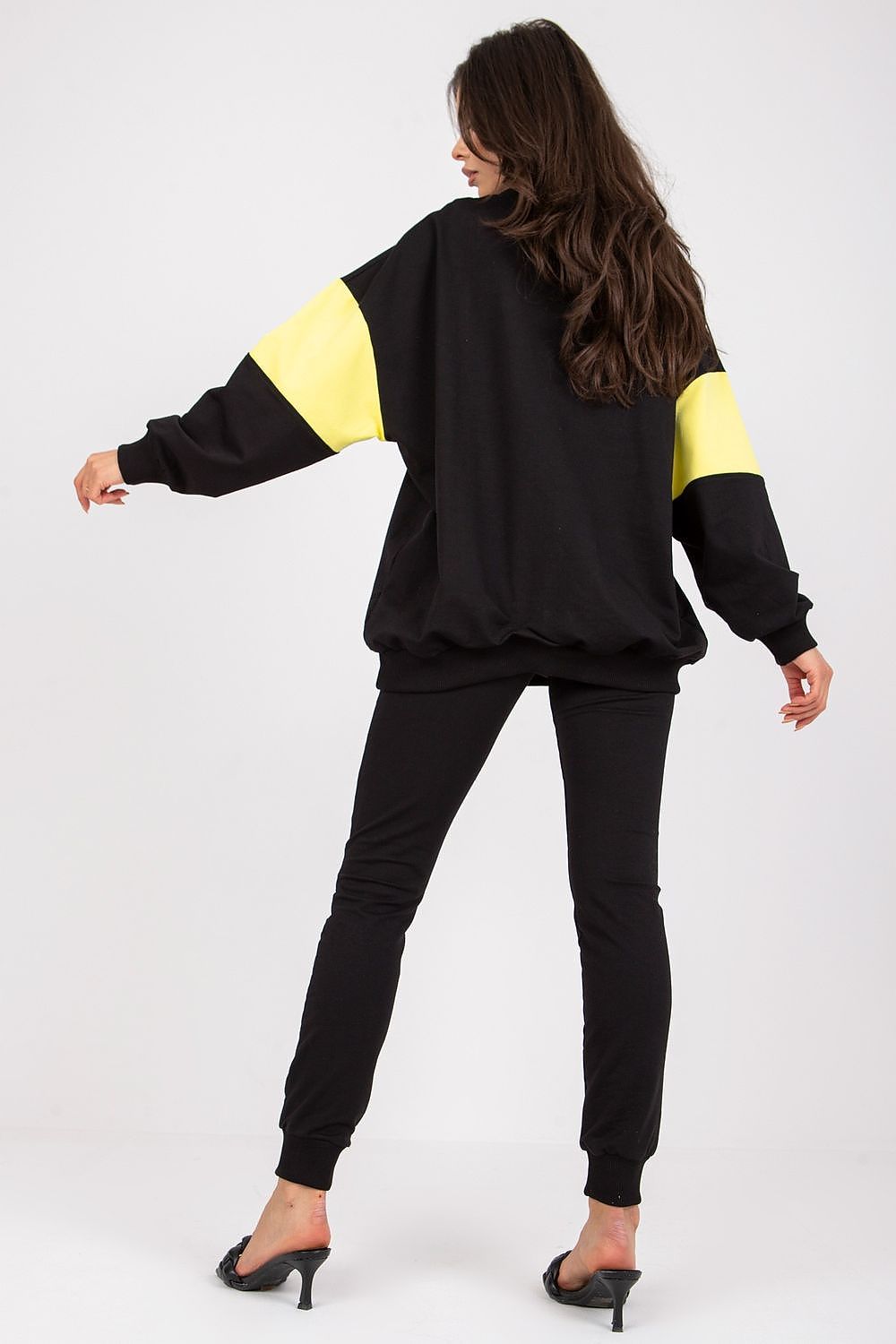 Chic luxury women's black tracksuit set displayed from the back, highlighting the oversized sweatshirt with yellow detailing and tailored pants. Stylish model demonstrates a perfect blend of comfort and elegance.