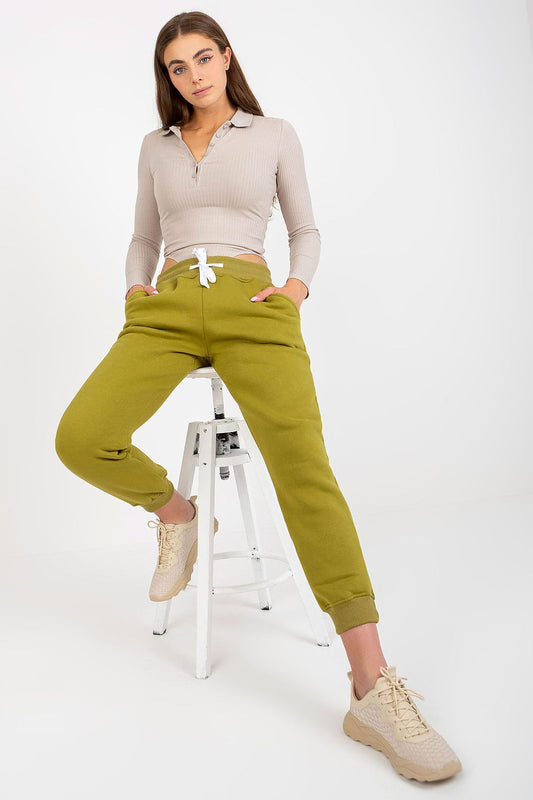 Elegant model showcasing luxurious cotton-spandex tracksuit trousers in olive green with waist tie and slip pockets, styled with a fitted ribbed top and stylish footwear.