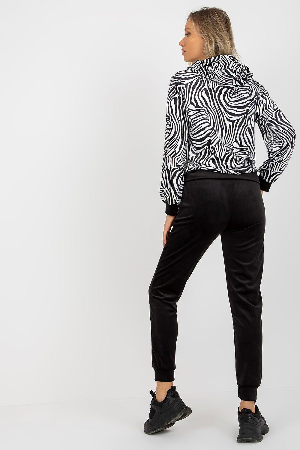 Elegant woman showcasing the luxurious Rue Paris velour set featuring a stylish animal print sweatshirt with a hood and chic black long pants, perfectly rounded off with sporty black sneakers.