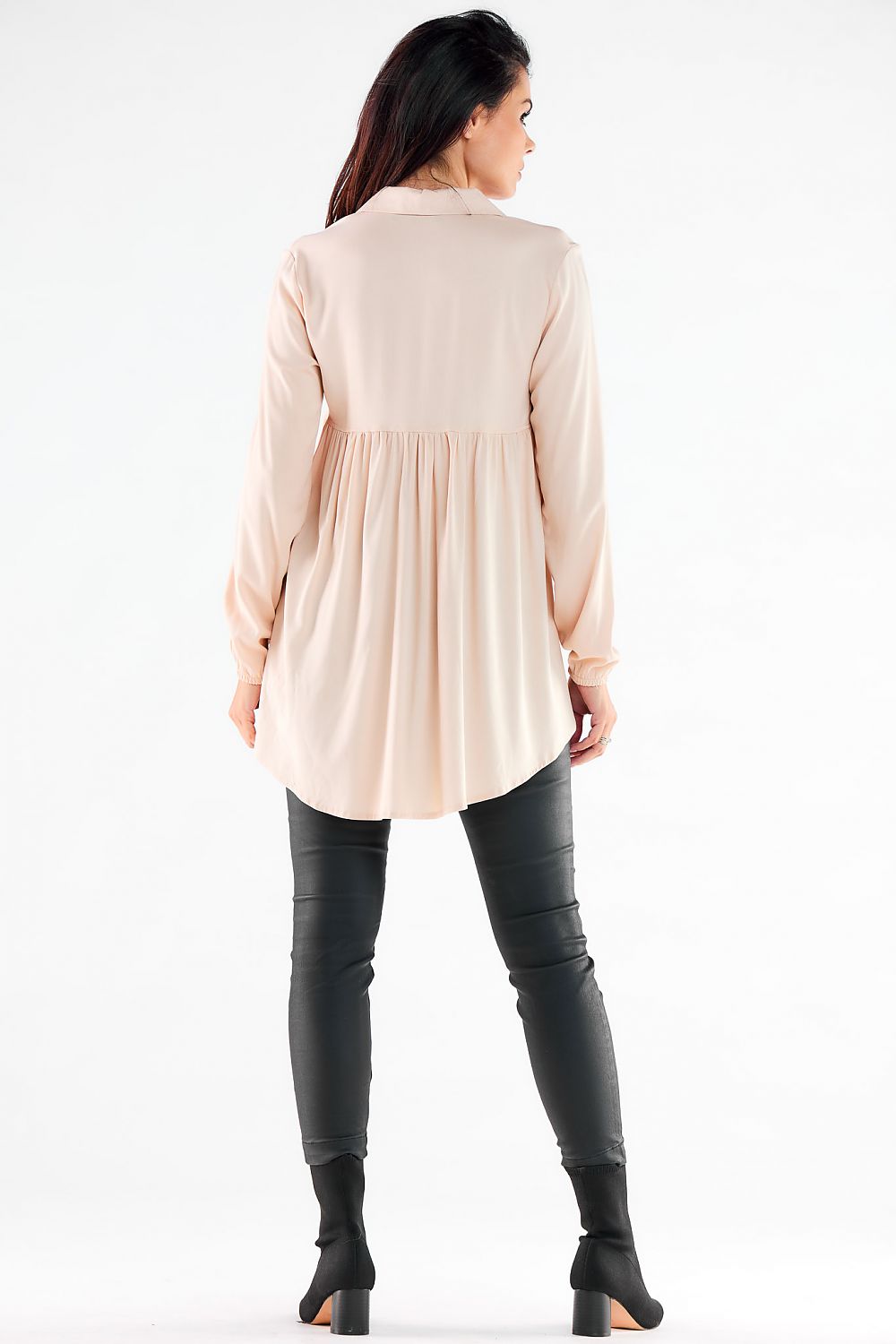 Rear view of a woman in an elegant long sleeve shirt featuring an extended back and gathered design, perfectly complemented by imitation leather pants, exuding effortless style.