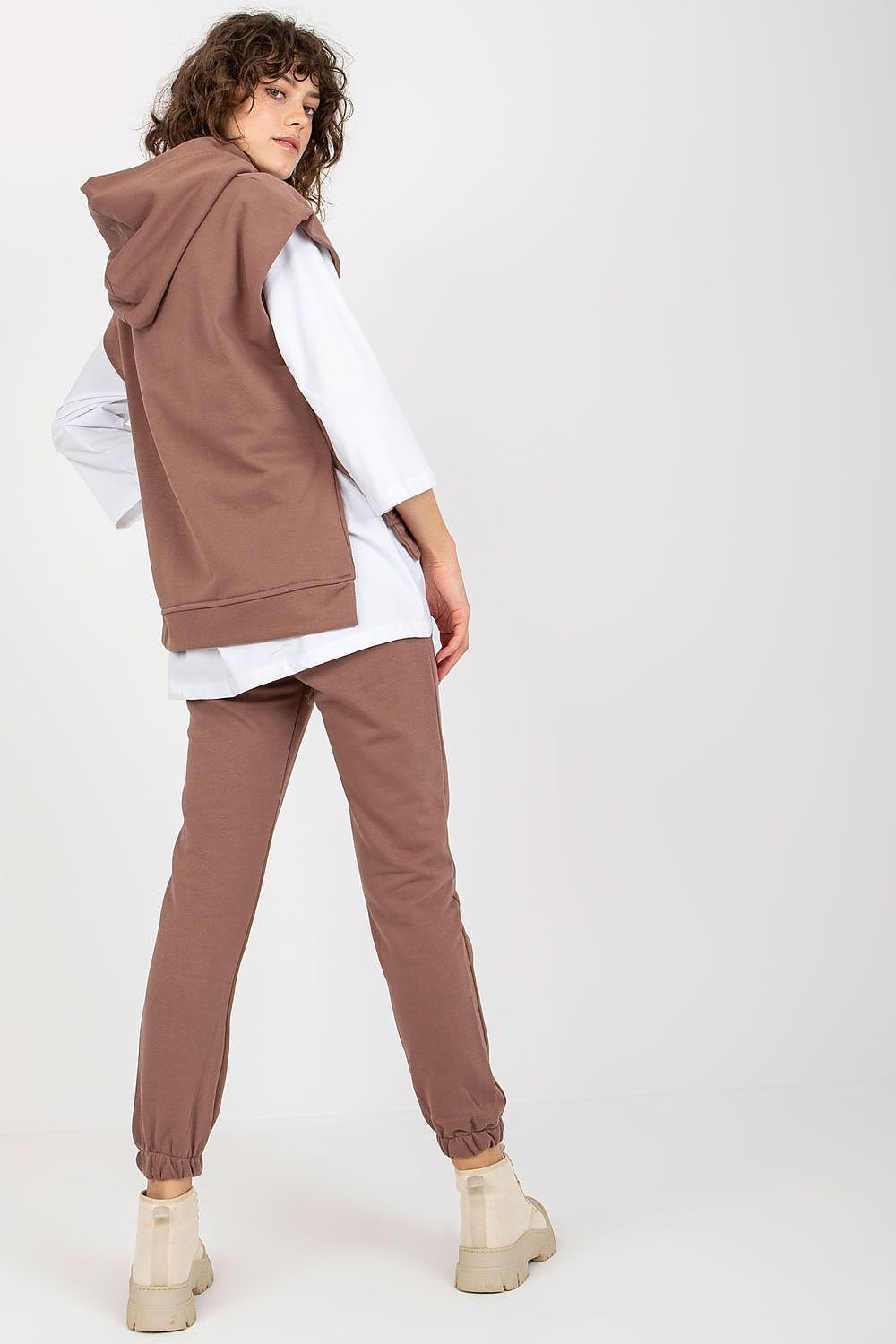 Refined model captured from the back in a luxurious brown sweatsuit set, featuring a relaxed-fit sleeveless hoodie over a long-sleeve blouse, presenting an effortless yet sophisticated look.