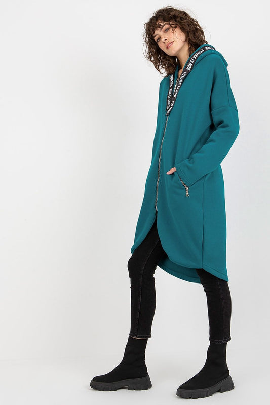 Chic women's zippered hooded sweatshirt with a stylish extended silhouette, showcasing a striking teal hue, complemented by fitted black pants and fashionable boots, ideal for a fashionable streetwear ensemble.