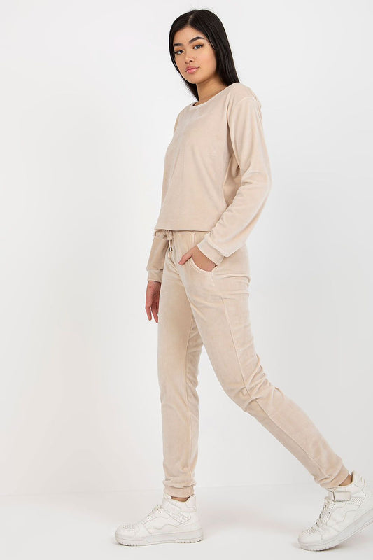 Elegant model showcasing a luxurious velour blouse and pants set in beige, featuring a tie waist and slip pockets, styled with white sneakers for a chic, casual look.