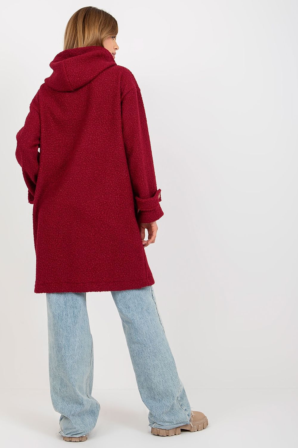 Back view of a woman elegantly dressed in a plush red coat with a hood, button closure, and loose denim, showcasing the luxurious and comfortable style.