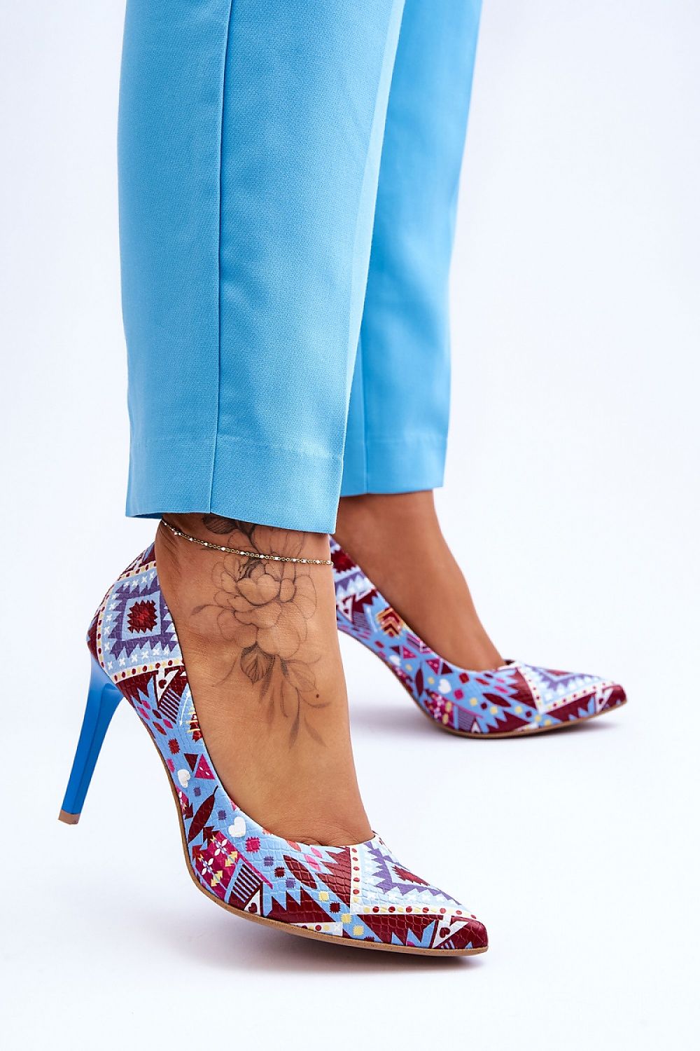 Close-up view of luxurious high heels for women by Step in Style, showcasing intricate patterns and a sophisticated stiletto heel, paired with elegant blue trousers.