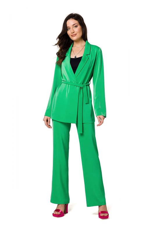 An elegant woman poses in a luxury green flowing jacket with matching trousers, crafted by Makover. The outfit's bold colour and unique design exude sophistication and trendiness.