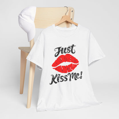 Stylish graphic tee featuring 'Just Kiss Me!' artwork with vivid red lips, elegantly draped over a chair alongside a white cap, ideal for casual outings.