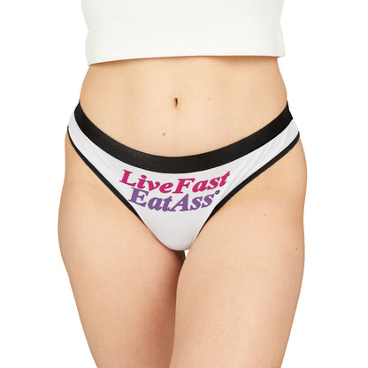 Model showcasing exquisite white thong panties with the phrase 'Live Fast Eat Ass' in vibrant pink and purple, embodying a bold, confident style.