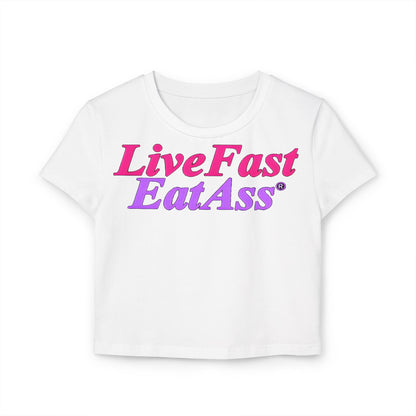 Chic white cropped T-shirt featuring the playful and sassy slogan 'Live Fast EatAss®' in vibrant hot pink and purple gradient. Perfect for adding a touch of bold style to any outfit.
