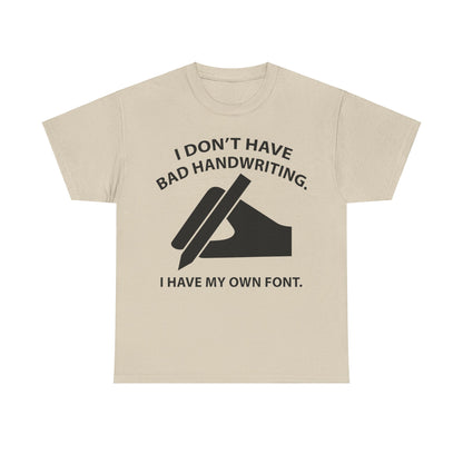 Luxury graphic unisex t-shirt featuring the phrase 'I DON'T HAVE BAD HANDWRITING. I HAVE MY OWN FONT.' with a stylish illustration of a hand gripping a pen, perfect for those who appreciate creative humour.
