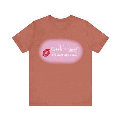 Sabrina Carpenter Inspired Unisex Short Sleeve Tee with Vibrant Lipstick Print in warm terracotta, elegantly featuring the phrase 'Short n' sweet i'm working Late...' complemented by a striking red lipstick kiss.