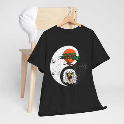 Chic black graphic t-shirt draped over a chair beside a baseball cap, featuring an eye-catching yin-yang design with a bonsai tree and eagle, reflecting a blend of humour and martial arts spirit.