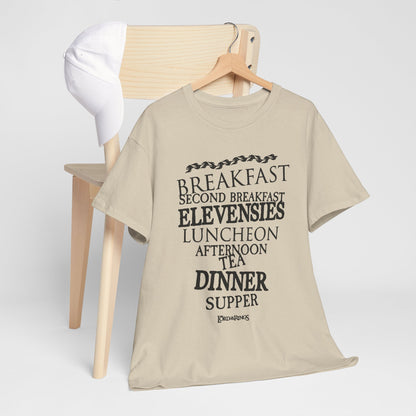 Luxurious graphic t-shirt featuring hobbit meal names in elegant typography, displayed artistically on a wooden chair with a white cap, perfect for casual chic styling.