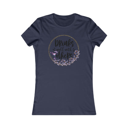 Elegant navy women's t-shirt emblazoned with the charming phrase 'Drinks well with others' encircled by a floral wreath and a cocktail motif, perfect for festive occasions.