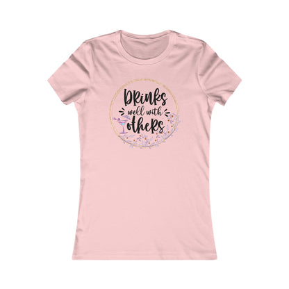 Elegant pink women's t-shirt featuring the phrase 'Drinks well with others' within a floral wreath design, complemented by a cocktail glass, ideal for casual gatherings.
