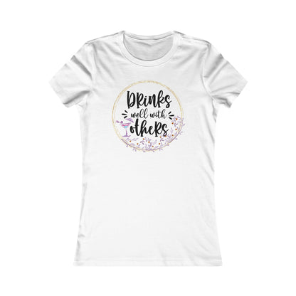 Chic white women's t-shirt featuring the elegant phrase 'Drinks well with others' surrounded by a floral wreath and a cocktail glass design, perfect for social gatherings.