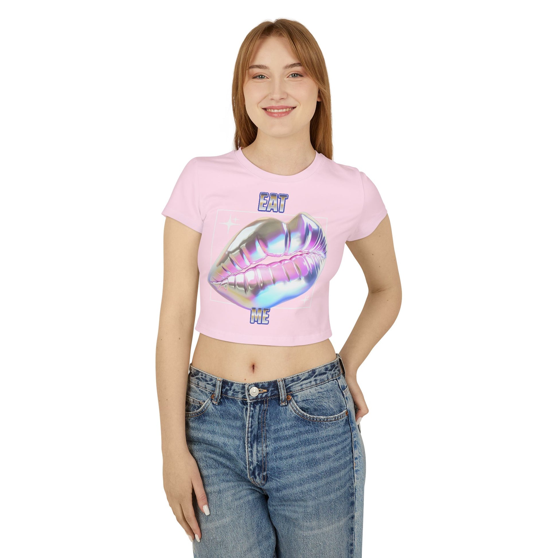Elegant model wearing the Cheeky Women's Cropped T-Shirt, showcasing the bold 'Eat Me' lips design in iridescent graphic against a pastel pink background, styled with high-waisted jeans for a chic look.