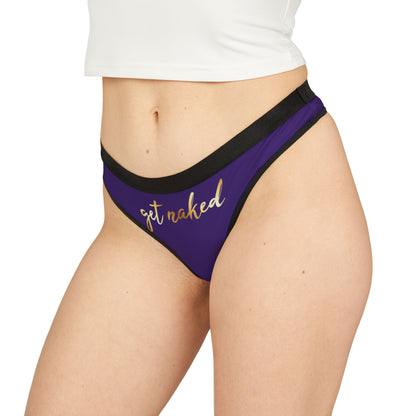 Chic model displaying a purple thong inscribed with 'get naked' in gold, accentuating playful elegance in lingerie.