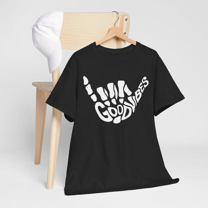 Sophisticated black men's T-shirt elegantly draped over a minimalist wooden chair, featuring a captivating white skeletal hand graphic with the phrase 'GOOD VIBES', complemented by a chic white cap.