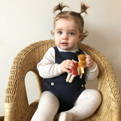 Infant wearing a Stylish Baby Girl Cotton Romper while holding dolls, highlighting luxury and comfort in a wicker chair.