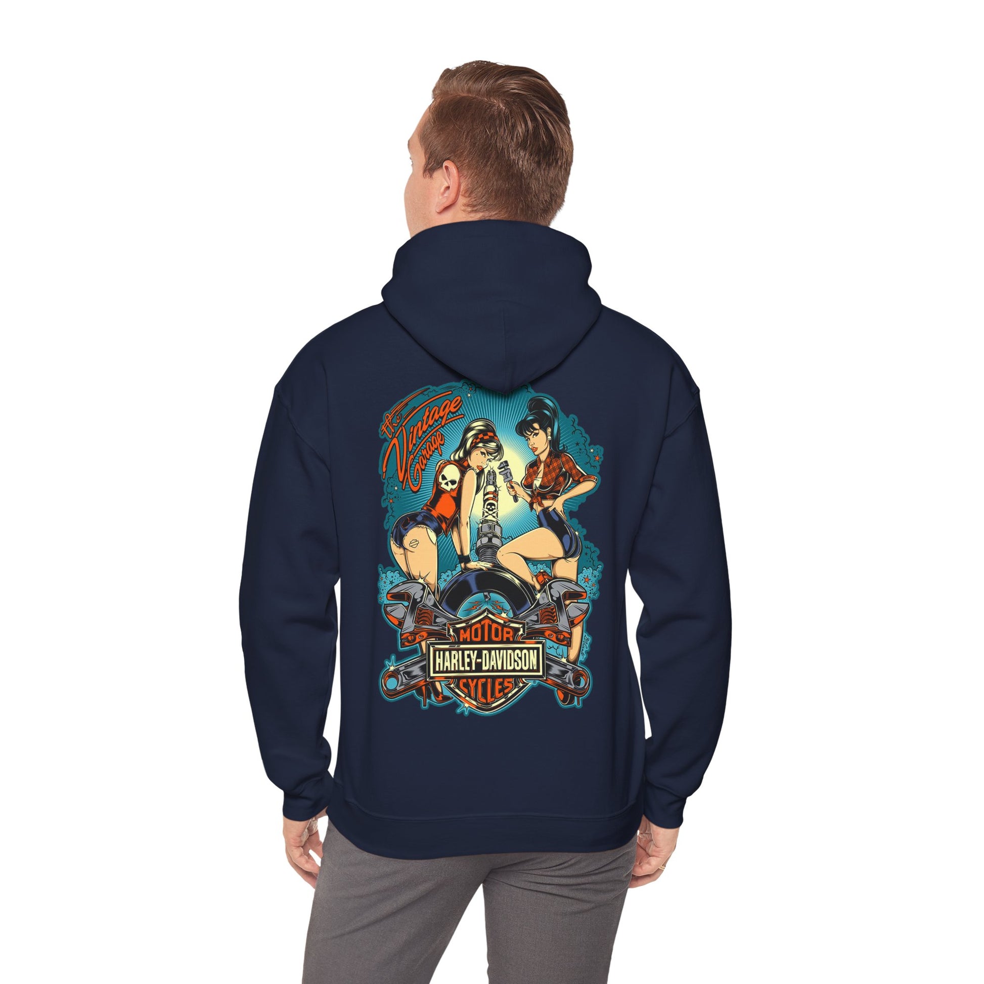 Stylish man wearing a navy hoodie with an artistic back print featuring two retro pin-up women working on a motorcycle, embodying classic vintage aesthetics.
