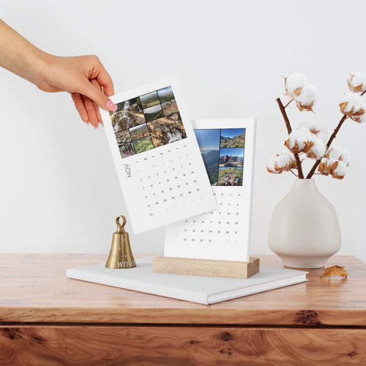 A hand placing a stunning nature photograph of the Marbella Hiking Club 2025 Vertical Desk Calendar, showcasing vibrant images for November.