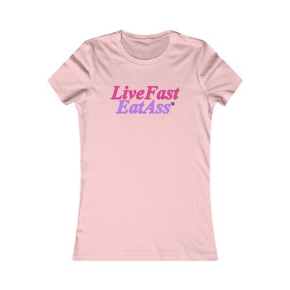 Stylish women's fitted t-shirt in soft pink, featuring the eye-catching slogan 'Live Fast Eat Ass®' in a dazzling gradient of pinkish-purple to hot pink, perfect for those who dare to express their bold spirit.