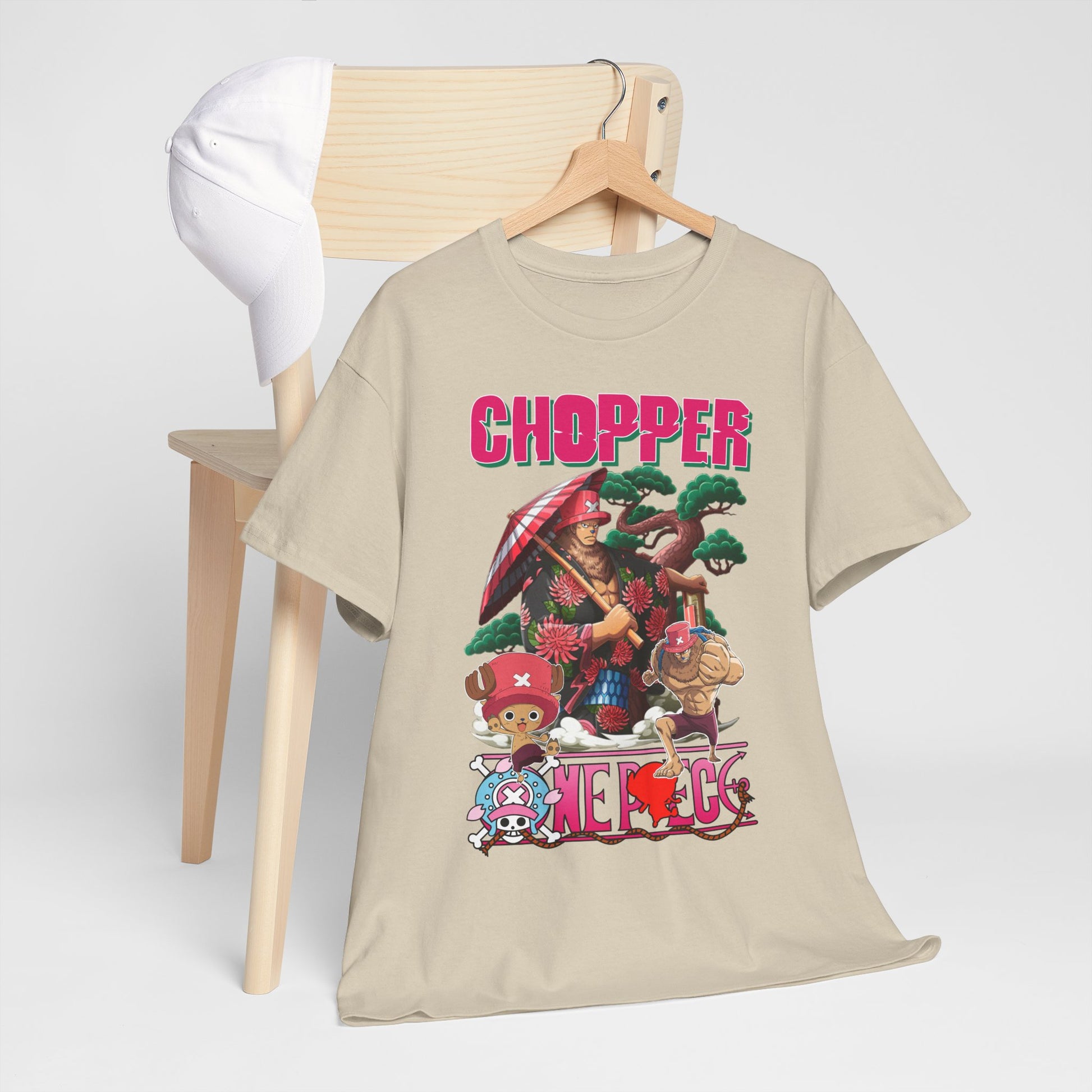 Charming beige graphic t-shirt adorned with an anime theme, featuring Chopper and friends, artfully arranged on a chair with a stylish cap.