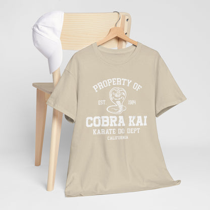 Fashionable styling of a Cobra Kai T-shirt draped on a chair with a white cap, highlighting the distinguished logo and premium fabric in a soft beige hue.