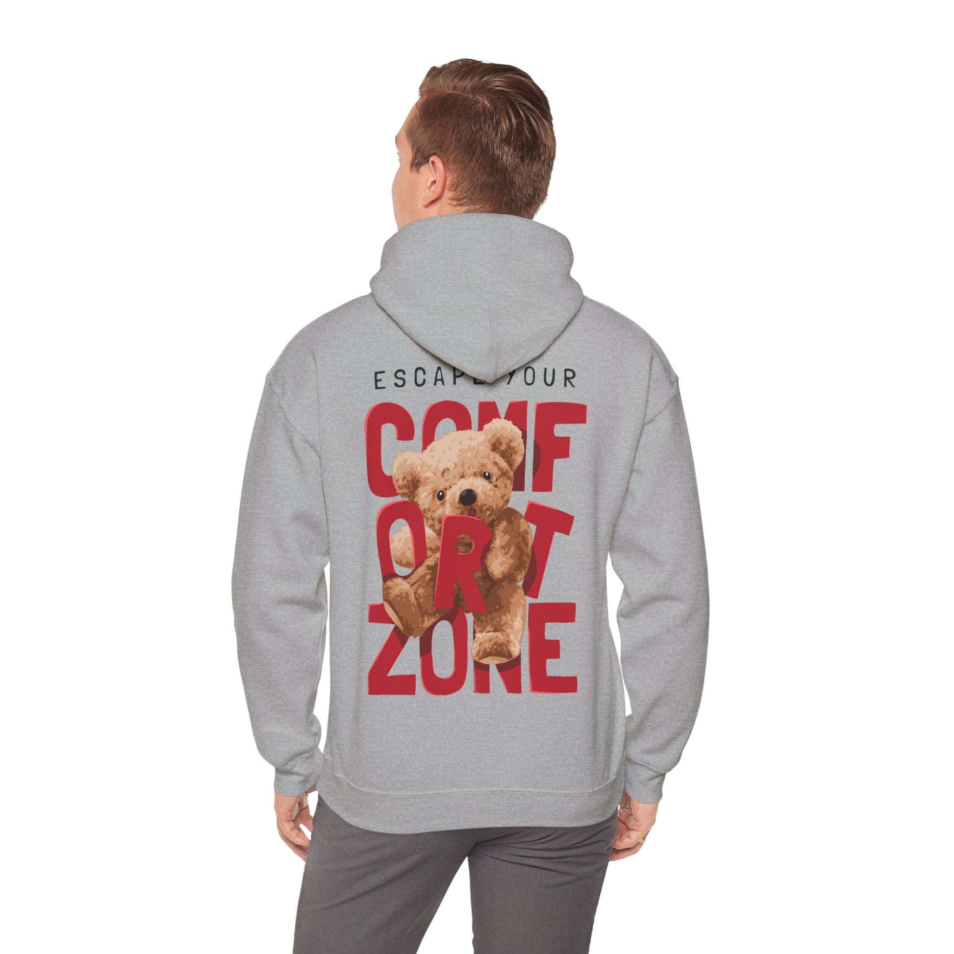 Model wearing a luxury grey hoodie with a bold back print reading 'ESCAPE YOUR COMFORT ZONE', featuring a playful teddy bear graphic, exemplifying contemporary fashion and comfort.